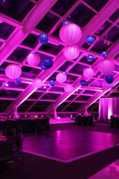 an empty dance floor is lit up with purple lights and paper lanterns hanging from the ceiling