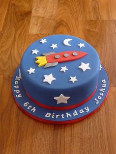 a blue birthday cake with white stars and a red rocket ship on top, sitting on a wooden table