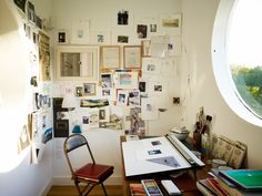 a room with a desk, chair and many pictures on the wall above it in front of a round window