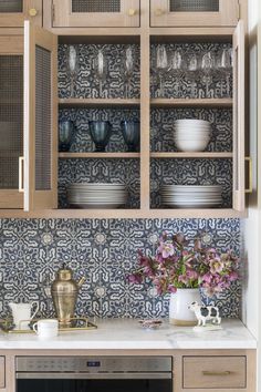 a kitchen with wooden cabinets and blue patterned wallpaper on the back splash, white countertops and silver appliances