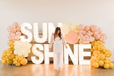 a woman standing in front of a sign that says sun shine with balloons all around her