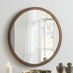 a round mirror sitting on top of a table next to a candle and vases