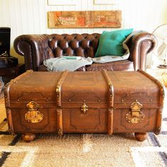 an old trunk is sitting on the floor in front of a leather couch and ottoman