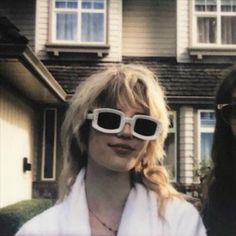 two women standing in front of a house with large sunglasses on their faces and one woman wearing white