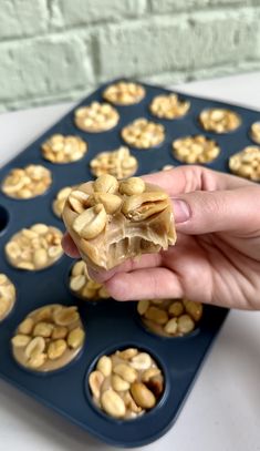 a person is holding some kind of food in front of a muffin tin with nuts on it