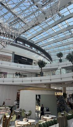 the inside of a shopping mall filled with lots of tables and chairs under a glass ceiling