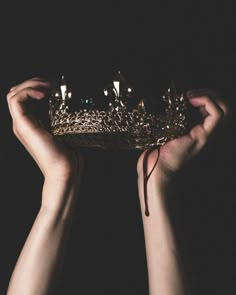 two hands holding a golden crown in the dark