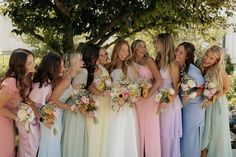 a group of women standing next to each other wearing dresses and holding bouquets in their hands