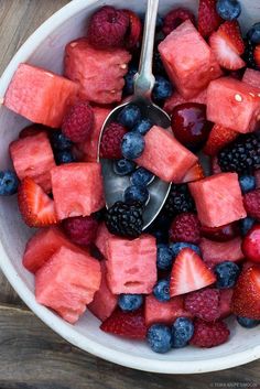 a bowl filled with watermelon cubes, raspberries and blueberries