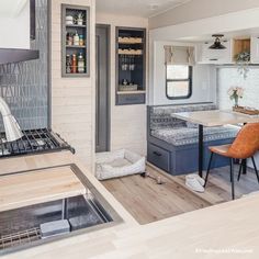 a kitchen and dining area in a small trailer with wood flooring, white walls and cabinets