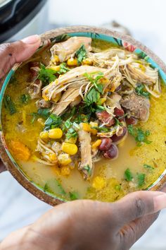 two hands holding a bowl of chicken and corn soup