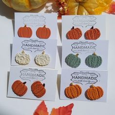 four different colored pumpkins are sitting on a table next to some autumn leaves and an acorn