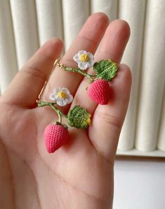 a hand holding three tiny crocheted strawberries with flowers on each one and daisies on the other