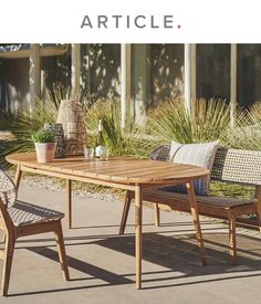 a wooden table with two chairs next to it and plants on the ground near by