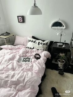 a bed with pink sheets and pillows in a room next to a lamp, mirror and other items