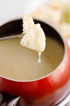 a piece of bread is being dipped into soup in a red saucepan on a white plate