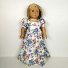 a doll with blonde hair and blue eyes wearing a floral dress, standing against a white background