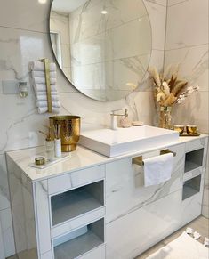 a white bathroom with marble counter tops and gold accents on the mirror above the sink