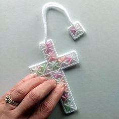 a hand is holding a crocheted cross ornament on a gray surface