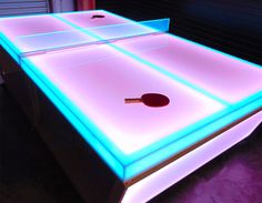 two ping pong tables lit up with blue and pink lights on them in a dark room