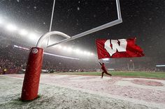 a man walking across a baseball field holding a red and white flag with the letter w on it