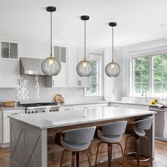 a large kitchen with white cabinets and marble counter tops, three pendant lights hanging over the island