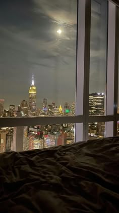 a view of the city at night from a bedroom with a large window overlooking it