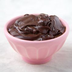 a pink bowl filled with chocolate frosting on top of a table