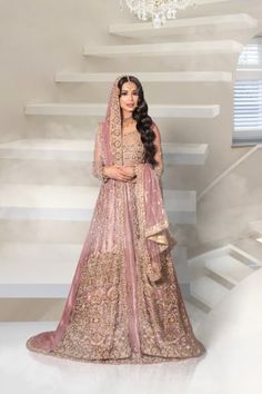 a woman in a pink and gold bridal gown standing next to some white stairs