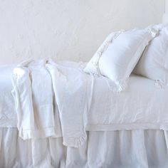 a bed with white linens and ruffled edges in front of a stucco wall