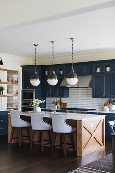 a large kitchen with blue cabinets and white stools in front of an island counter