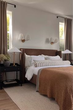 a large bed sitting next to two lamps on either side of a window in a bedroom