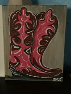 a painting of a pair of pink cowboy boots on a wooden block with blue wall in the background