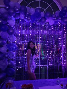 a woman standing in front of a purple backdrop with balloons and streamers on it