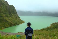 a woman standing on top of a lush green hillside next to a body of water