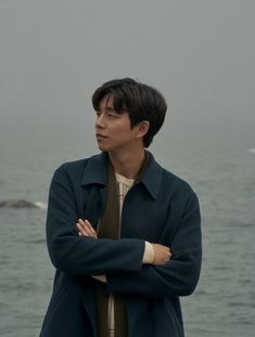 a man standing in front of the ocean with his arms crossed and looking off into the distance