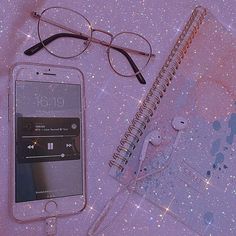 an iphone, glasses, and notebook on a table with glittery paper around it