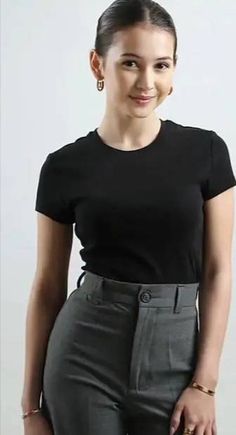 a woman in black shirt and grey pants posing for the camera with her hand on her hip