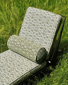 an outdoor chaise lounge in the middle of some tall grass, with a roll of fabric covering it