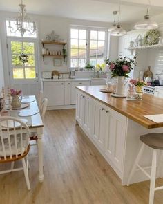 a white kitchen with wooden counter tops and chairs in front of the stove top oven