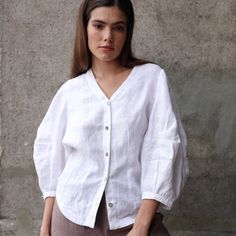 "Stylish Balloon Sleeve Linen Blouse with a modern oversized look. Featuring exaggerated puff sleeves, a V-neck design, and a comfortable ¾ sleeve length. Perfect to pair with simple bottoms for a chic and contemporary style. DETAILS ⚬ V-neckline. ⚬ Front button closure. ⚬ 3/4 puff sleeves. ⚬ Cocoon Back. ⚬ Made of washed organic Oeko-Tex certified linen. ⚬ The linen is NOT see-through. ⚬ Shown here in White.  FIT / SIZE ⚬ Designed for a loose fit.  If you would like to add or subtract 10cm from the length, let us know. ⚬ Handmade to order (can be made-to-measure, please write down your measurements in the personalization box) ⚬ Sizes XXS to XL (please see detailed size chart in photos). MODEL'S MEASUREMENTS ⚬ The model is wearing a size XS. ⚬ The model's measurements are Bust 34½\" (88 cm Oversized Blouse With Blouson Puff Sleeves, Casual Oversized Blouse With Puff Sleeves, Oversized Puff Sleeve Top For Work, Balloon Sleeve Tops With Button Cuffs For Daywear, Daywear Puff Sleeve Top With Relaxed Fit, Oversized Blouse With Blouson Balloon Sleeves, Lantern Sleeve Tops With Button Cuffs For Daywear, Spring Oversized Blouse With Puff Sleeves, Oversized Blouse With Gathered Sleeves For Spring