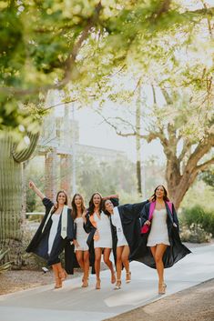 four young women in graduation gowns are walking down the street with their arms in the air