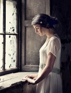 a woman standing in front of a window with her hands on the ledge and looking out