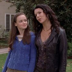 two young women standing next to each other in front of a house with trees and bushes