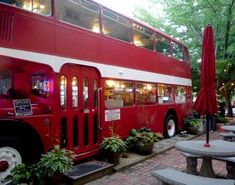 a red double decker bus parked next to tables and umbrellas