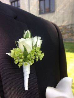 a boutonniere with white roses and green leaves on it is sitting in the lapel of a suit