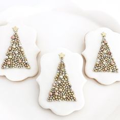 three decorated cookies are on a plate with white frosting and gold beads in the shape of a christmas tree