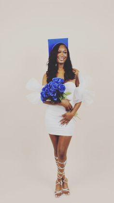 a woman in a white dress holding a bouquet of flowers and a blue graduation cap on her head