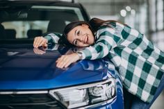 a woman leaning on the hood of a blue car with her arms resting on it