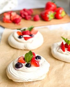 three small pastries with fruit on them sitting on top of a wooden cutting board